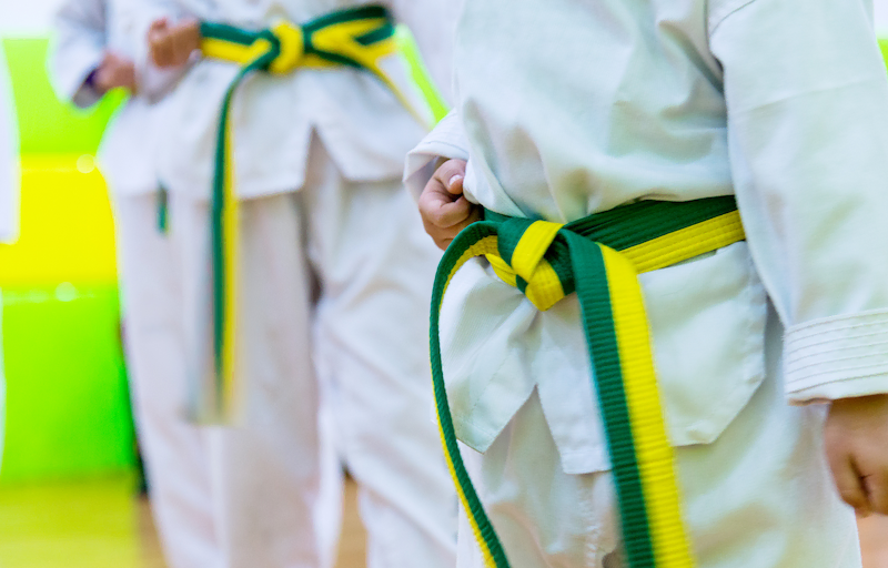 un enfant en uniforme de taekwondo appelé dobok et une ceinture verte et jaune en position de garde avec les poings fermé lors d'un entrainement avec d'autres enfants de son niveau